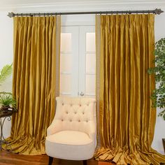 a white chair sitting in front of a window covered in gold drapes next to a potted plant