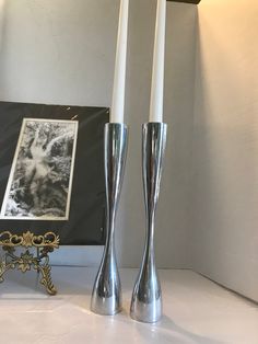 two silver candles sitting on top of a table next to a framed photo and candle holder