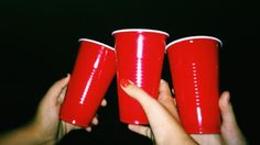 three red cups being held by two hands in front of a black background with white dots