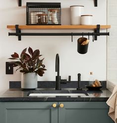 a kitchen with green cabinets and black counter tops is pictured in this image, there are plants on the shelves above the sink