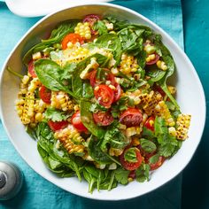 a salad with corn, tomatoes and spinach in a white bowl on a blue table cloth