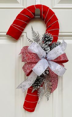 a christmas wreath with pine cones and ribbons hanging on a door