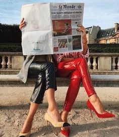 a woman sitting on a bench reading a newspaper while wearing red pants and high heels