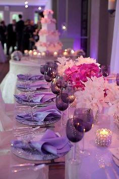 the table is set up with purple and white flowers, silverware, and candles