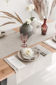 a table set with place settings and flowers in vases on the table top, along with napkins