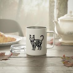 a white coffee mug with a skeleton cat design on it sitting on a wooden table