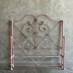 a pink iron bed frame against a gray wall with white trimmings and circles on the headboard