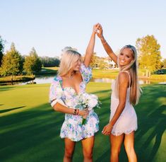 two beautiful young women standing next to each other on top of a lush green field