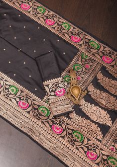 This breathtaking black saree showcases a contemporary interpretation of Banaras' classic weaving techniques. Adorned with intricate chunri zari buttas throughout the body, it is accompanied by a vibrant meenakari Zari floral border and pallu, infusing the luxurious silk fabric with a pop of color. If you admire a unique blend of design, texture, and shades, this saree will captivate your senses. SILK MARK CERTIFIED This saree is ready to wear with fall and pico done. Handmade silk tassels adorn the pallu and add more grace to it. An unstitched blouse fabric is included. *Note: There may be minor variations in the shade, the texture of the product. Hues/textures show differently due to variations in screen settings and other factors, *Note: This saree is woven of pure natural silk, there m Black Art Silk Pre-draped Saree With Zari Weaving, Designer Black Banarasi Silk Saree, Black Kurta With Cutdana Traditional Drape, Traditional Black Pre-draped Saree, Black Pre-draped Saree With Traditional Patterns, Transitional Black Pre-draped Designer Saree, Designer Black Tussar Silk Saree, Black Dupatta With Zari Weaving For Designer Wear, Black Pre-draped Saree With Zari Weaving In Art Silk