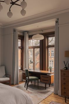 a bedroom with a bed, desk and chair in it next to two large windows