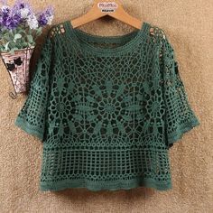 a green crocheted top with flowers hanging on a hanger next to it