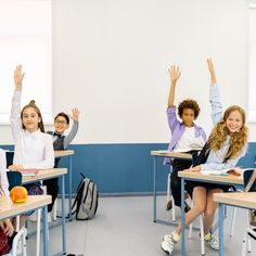 there are many children sitting at desks raising their hands