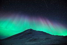 the aurora bore is seen in the sky above a snowy mountain with green and purple lights