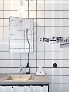 a bathroom sink sitting under a mirror next to a white tiled wall with pictures on it