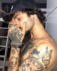 a man with tattoos on his arms and chest covers his face while wearing a hat