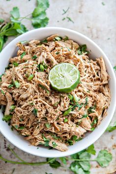 a white bowl filled with shredded chicken and garnished with cilantro, green onions and a lime