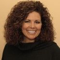 a woman with curly hair wearing a black hoodie smiling at the camera while standing in front of a wall