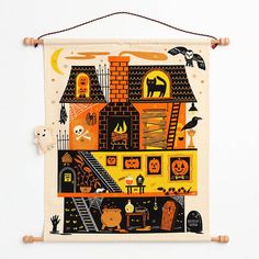 a wall hanging with halloween decorations on it and a cat sitting in front of the house