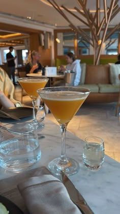 two martini glasses sitting on top of a table next to another glass filled with liquid