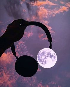 a hand holding an object in front of a full moon with clouds and pink hues