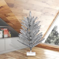 a silver christmas tree sitting on top of a wooden floor next to a book shelf