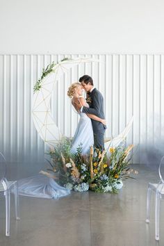 a bride and groom standing in front of a white moon with flowers on the floor