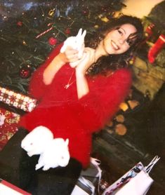 a woman in a red sweater is holding a white cat and posing for the camera