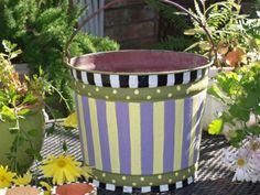 a purple and white striped bucket sitting on top of a table next to potted plants