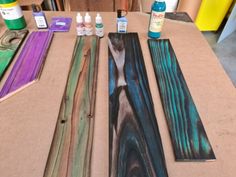 several different colored wood planks sitting on top of a table next to paint bottles