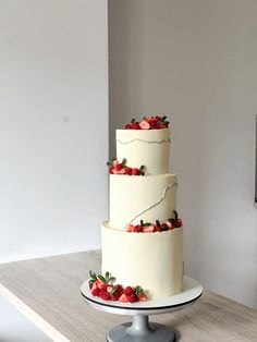 a three tiered cake with strawberries on the top is sitting on a table