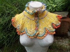 a white mannequin wearing a yellow crocheted collar with multicolored buttons