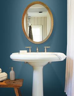 a white pedestal sink sitting under a mirror in a bathroom next to a wooden stool