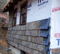 a house under construction with siding on the roof and windows being installed in front of it