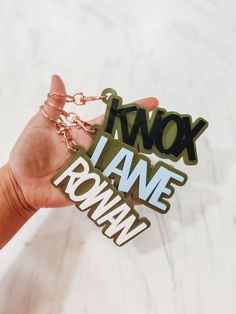 a hand holding two key chains with the words iwox i have roman written on them