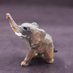 an elephant figurine made out of wood on a purple carpeted floor with one trunk sticking out