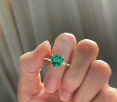 a woman's hand holding a ring with a green heart shaped stone on it