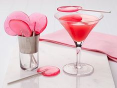 two cocktail glasses with red liquid in them on a white table cloth and pink napkins