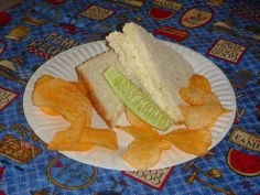 a paper plate topped with a sandwich and chips on top of a blue table cloth