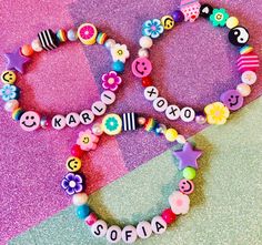 two colorful bracelets with name beads and smiley faces on them sitting on a purple background