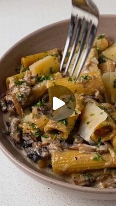 a bowl filled with pasta and mushrooms on top of a white countertop next to a fork