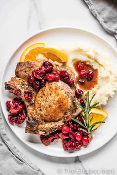 a white plate topped with meat, mashed potatoes and cranberries next to orange slices