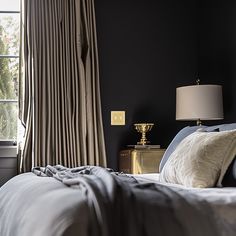 a bedroom with black walls and white bedding, gold nightstands and lamps on either side