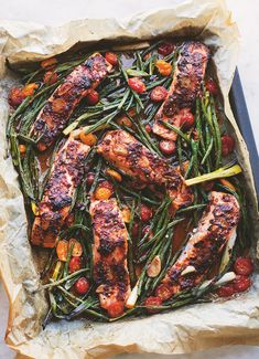 salmon, green beans and tomatoes in a pan on top of parchment paper with a knife