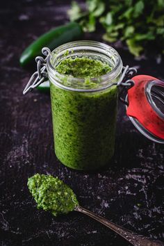 a jar filled with green pesto next to a spoon