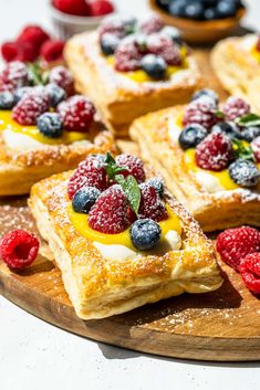 desserts are arranged on a wooden platter with raspberries and blueberries