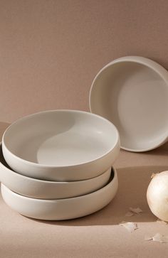 three white bowls and one onion are on the table