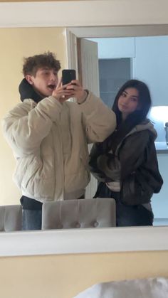 a man and woman standing in front of a mirror taking a selfie with a cell phone