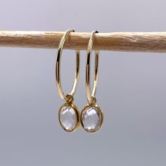 Clear quartz (rock crystal) oval crystal gemstone (7x9mm) drop earrings on 22 Carat gold vermeil medium hoop (20mm wide) sleeper ear wires. Sleeper ear wires are tubular in design with one end slotting a little into the other to form an endless ring. They are lightweight and uncomplicated. Vermeil is a high quality form of gold plating in which a thick layer of gold (this must be more than 2.5 microns and between 14 Carat and 22 Carat) is coated over 925 Sterling Silver. Shipped inside a white l Gold Faceted Teardrop Hoop Earrings, Handmade Paper Boxes, Quartz Rock, 22 Carat Gold, Wedding Gifts For Bridesmaids, Les Chakras, Rock Crystal, March Birth Stone, Crystals And Gemstones