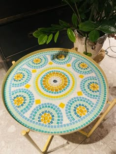 a table that has a mosaic design on it and is next to a potted plant