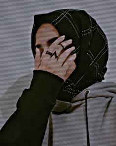 a person wearing a hoodie covering their face with his hands and looking at the screen